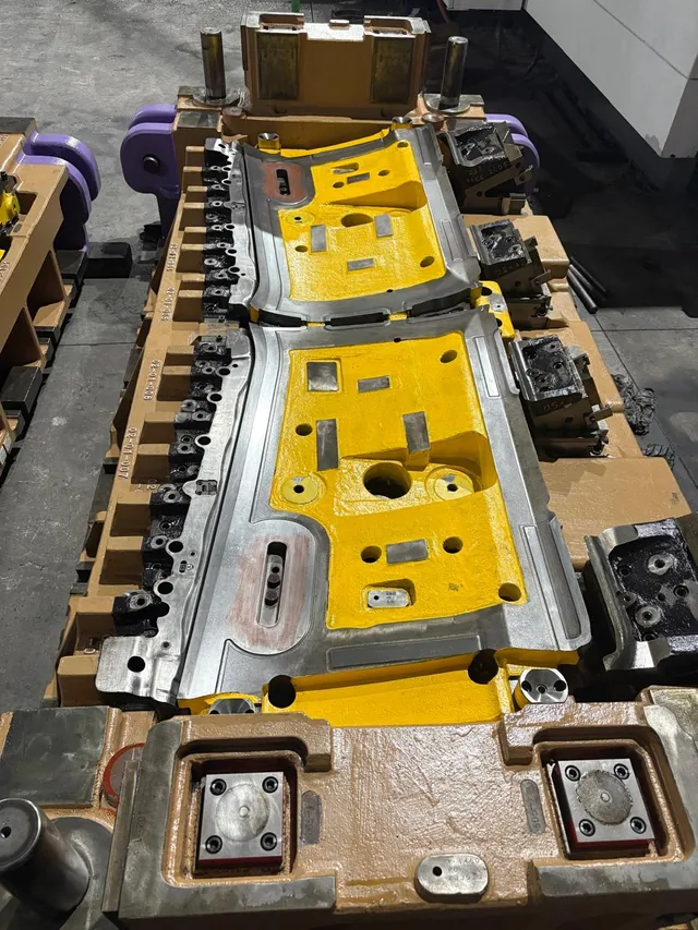 A twin station press tool with yellow die faces, seen along its length from one end